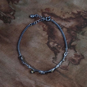 Organiskt kvistarmband i oxiderat sterlingsilver: Elegant kedja med peridot- och blomdetaljer