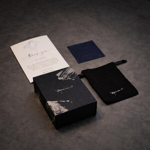 Puede incluir: Una caja negra con detalles de pinceladas blancas y el texto "Empress 147" se encuentra junto a una bolsa negra con cord&oacute;n con el mismo texto. Tambi&eacute;n se ve una tarjeta de agradecimiento y un pa&ntilde;o de limpieza azul marino.