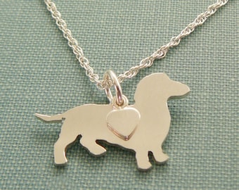 May include: A silver necklace with a dachshund silhouette charm and a small heart charm. The chain is a delicate rope style.