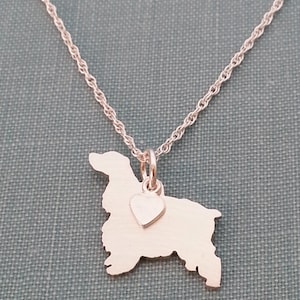 Peut inclure: Collier en argent avec un pendentif en forme de cocker et un petit pendentif en forme de cœur. Le collier est sur une chaîne en argent.