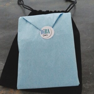 May include: A light blue envelope with a white circle sticker that says "DiBA DoG" in black text.