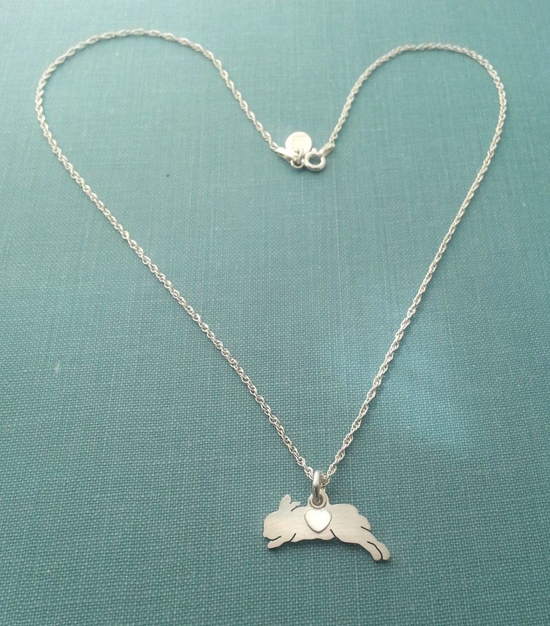 May include: A silver necklace with a delicate chain and a pendant shaped like a jumping rabbit with a small heart on its chest.