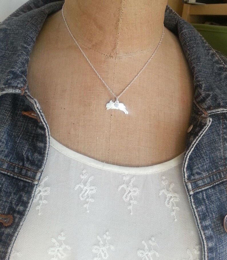 May include: A silver necklace with a delicate chain and a pendant shaped like a leaping rabbit. The pendant has a small heart cutout in the center.
