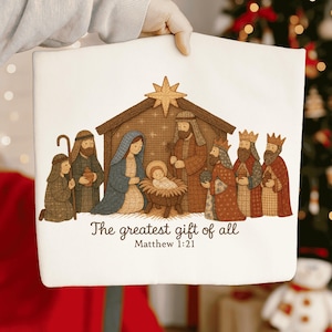 May include: A white rectangular pillow with a Nativity scene illustration. The image depicts Mary, Joseph, baby Jesus, and the Three Wise Men. Text reads "The greatest gift of all" and "Matthew 1:21".