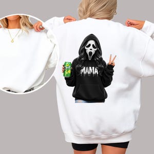 May include: White sweatshirt with a graphic of a Scream-style character wearing a black hoodie with the word "MAMA" and holding a green can. The character is making a peace sign.