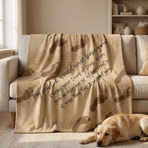 May include: A tan fleece blanket featuring a repeating pattern of dark brown footprints and the printed text: My child, I would never leave you. During your times of trial, when you see only one set of footprints, it was then that I carried you.