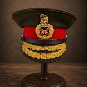 May include: An olive green military peaked cap featuring a vibrant red band, a dark brown leather chin strap, and gold embroidered oak leaf detailing on the visor. A prominent gold and red embroidered crest with a lion sits on the front band.