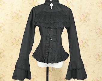 May include: Black long-sleeved blouse with a high collar and ruffled details. The blouse features a lace yoke, button-down front, and flared sleeves with lace trim. A decorative brooch accents the collar. The blouse is displayed on a mannequin.