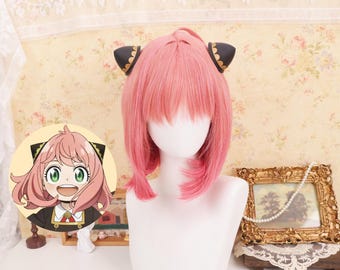 May include: A pink wig with bangs and black cat ear headbands on a white mannequin head. The wig is styled to resemble a character from an anime series. A cartoon image of the character is in the background.