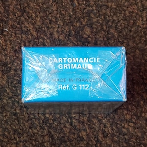 Puede incluir: Una caja azul con el texto "CARTOMANCIE GRIMAUD" y "R&eacute;f. G 112" impreso en ella. La caja est&aacute; envuelta en pl&aacute;stico.