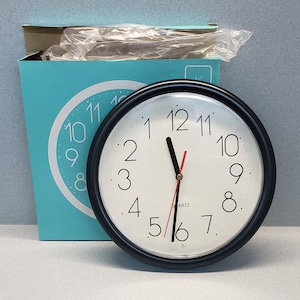 May include: A black framed clock with white face and black numbers. The clock has a red second hand and gold hour and minute hands. The clock face says "QUARTZ".