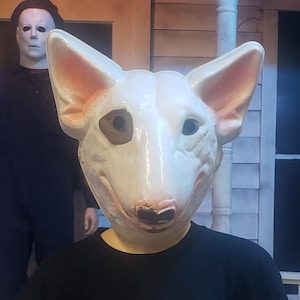 May include: A white dog mask with black eyes and a pink nose. The mask is made of a soft, pliable material and has a realistic look.