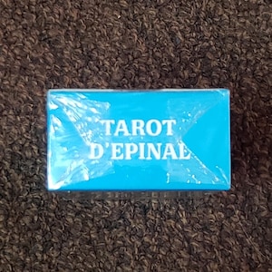 Puede incluir: Una caja azul con el texto "Tarot d'Epinal" impreso en blanco.