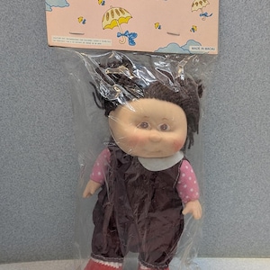May include: A vintage doll named "Ann & Bob" in a plastic package. The doll has dark hair, a pink and white polka dot shirt, brown overalls, and red shoes. The packaging features illustrations of umbrellas and the text "Little Ann & Bob".