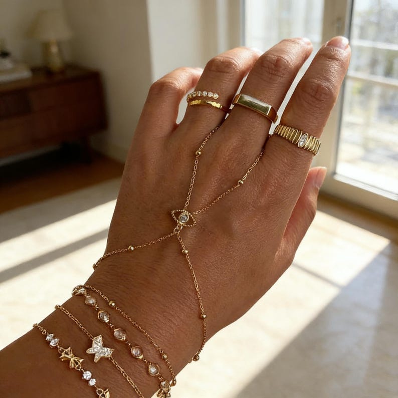 May include: Gold-toned jewelry set featuring multiple rings and bracelets. The rings include a band with small stones, a rectangular signet ring, and a ribbed ring with a central stone. Bracelets include star and butterfly designs, and a hand chain.