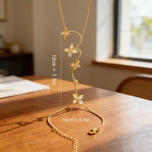 May include: A gold-colored hand chain with a delicate butterfly design. The chain features a necklace portion with a series of butterfly accents and a bracelet section connected by a chain. The necklace portion is 10 cm (3.9 in) long, and the bracelet is 16 cm (6.3 in).