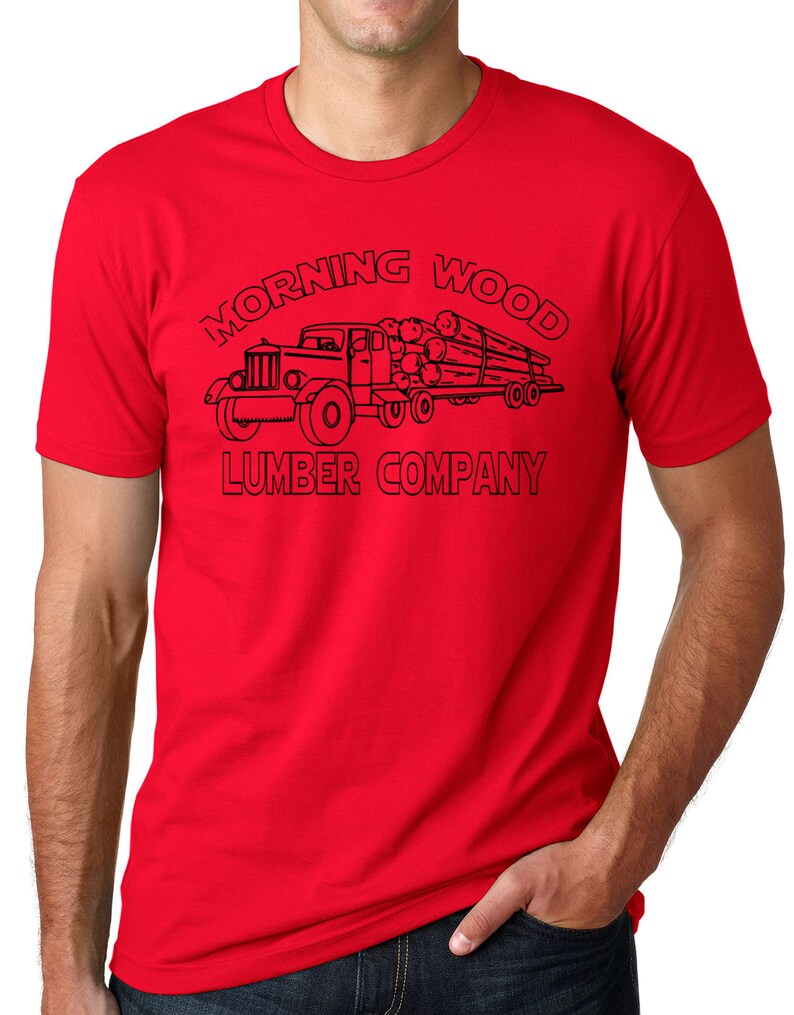 May include: A red t-shirt featuring a black graphic of a vintage logging truck hauling logs. The text "MORNING WOOD LUMBER COMPANY" is arched above and below the truck illustration. The shirt is made of a soft material.