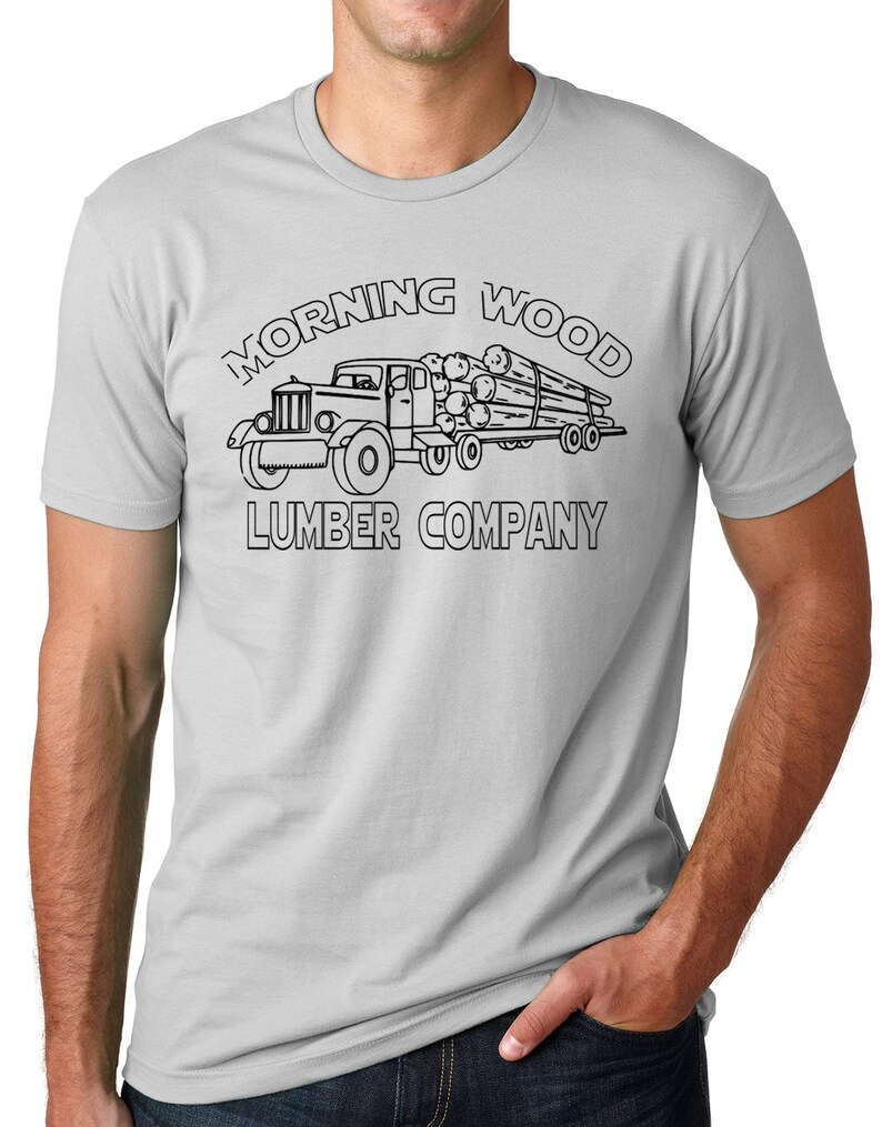 May include: A light gray t-shirt featuring a black graphic of a vintage truck hauling logs. The text "MORNING WOOD LUMBER COMPANY" is arched above and below the truck illustration.