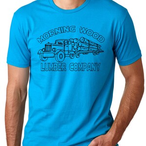 May include: A turquoise t-shirt featuring a black graphic of a vintage lumber truck carrying logs. The text "MORNING WOOD LUMBER COMPANY" is arched above and below the truck illustration.