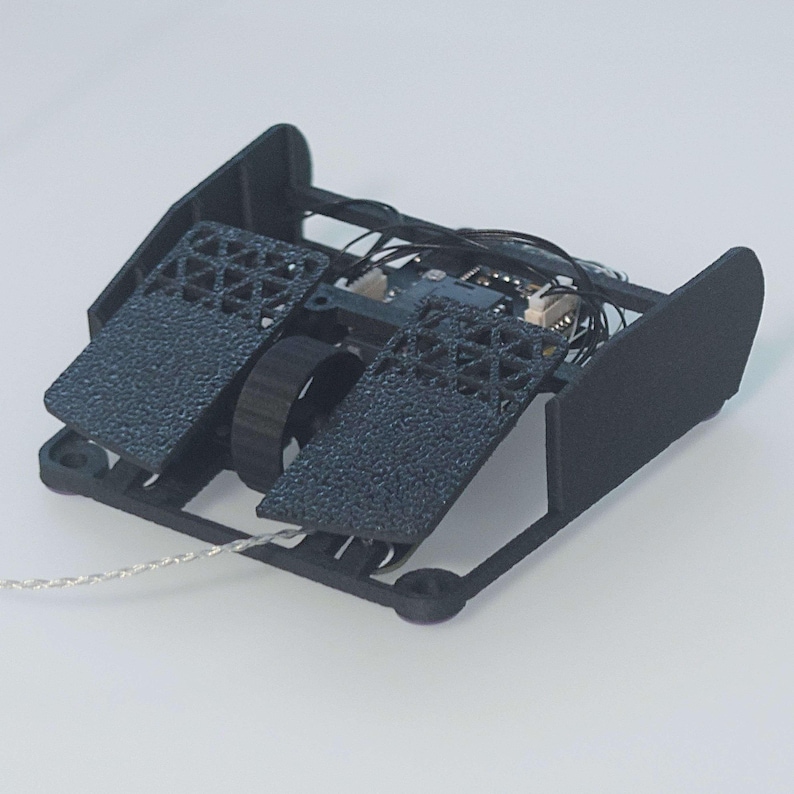 May include: A black 3D printed robot with a wheel and two textured pads. The robot is connected to a thin silver cable.