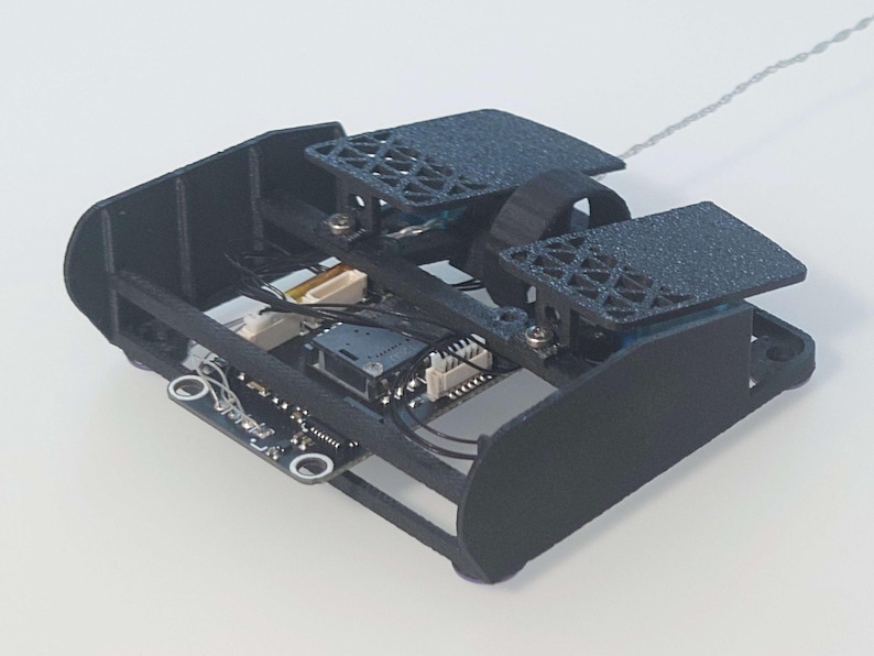 May include: A black 3D printed robot with a circuit board and wires visible. The robot has two wheels and a small camera.