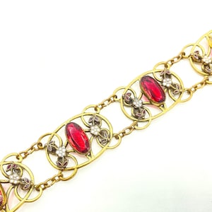 May include: A gold bracelet with a chain link design and red oval-shaped gemstones set in ornate floral motifs.