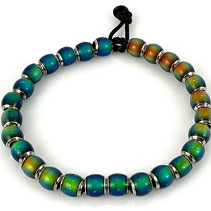 May include: A bracelet with iridescent green, blue, and orange beads with silver accents. The bracelet has a black elastic cord with a knot closure.