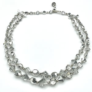 May include: A two-strand silver-toned necklace with clear, faceted beads. The necklace features a variety of bead shapes, including round, faceted, and geometric. The clasp is a simple hook and eye closure.