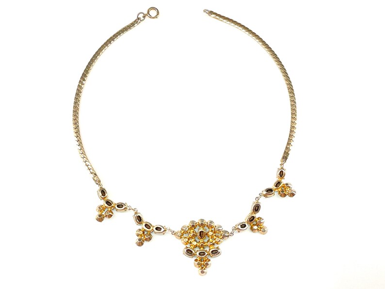 May include: A gold chain necklace with a cluster of small, clear and amber-colored stones in the center and smaller clusters of stones dangling from the sides.
