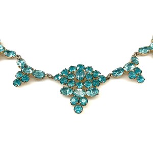 May include: A vintage necklace with a gold chain and a large cluster of turquoise blue rhinestones in the center. The necklace has three smaller clusters of turquoise blue rhinestones hanging from the center cluster.
