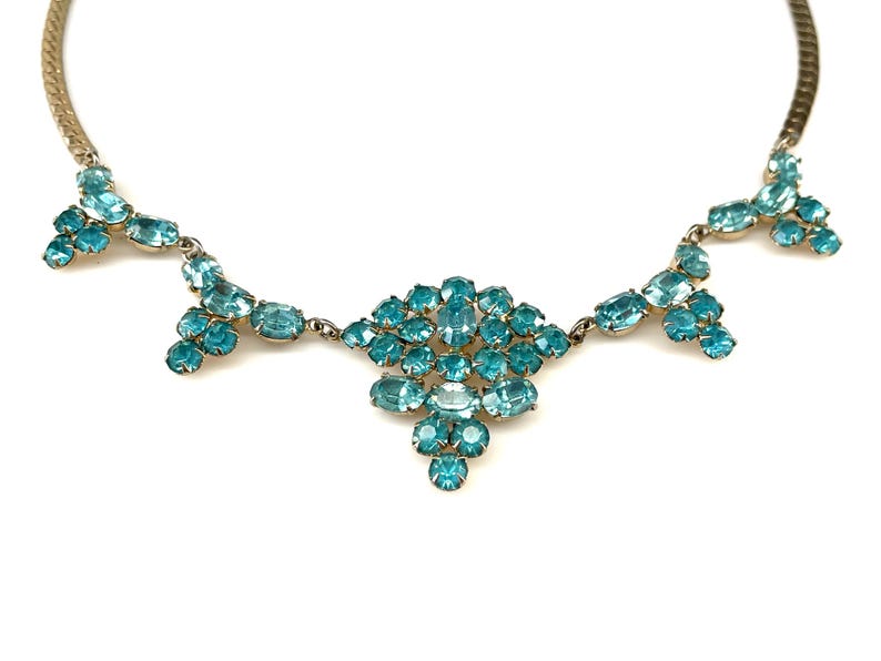 May include: A vintage necklace with a gold chain and a large cluster of turquoise blue rhinestones in the center. The necklace has three smaller clusters of turquoise blue rhinestones hanging from the center cluster.
