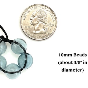 May include: A strand of six light blue glass beads with a black stripe around each bead. The beads are strung on a black elastic cord. A US quarter is shown for size comparison. 10mm Beads (about 3/8" in diameter)
