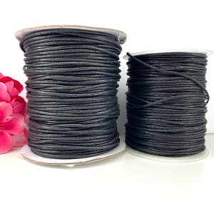 May include: Two spools of black waxed cotton cord. The spools are different sizes.