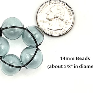 14mm hollow gray blue glass beads sit on a flat white surface next to a US quarter to show size.  These lampwork bubble beads have two holes and are grey with a light blue cast.