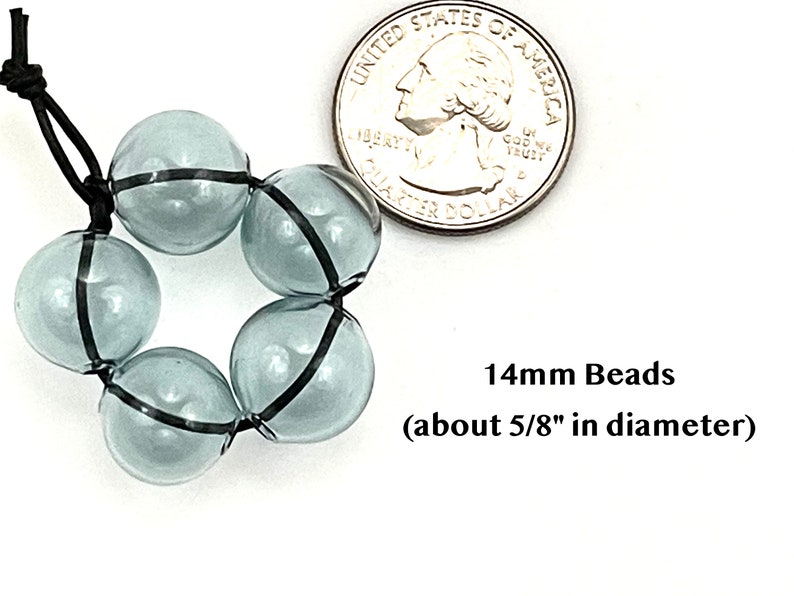 14mm hollow gray blue glass beads sit on a flat white surface next to a US quarter to show size.  These lampwork bubble beads have two holes and are grey with a light blue cast.