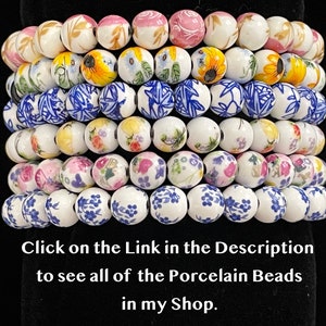 Pu&ograve; includere: Una collezione di perline rotonde in porcellana con vari disegni floreali e geometrici. Le perline sono bianche con dettagli dipinti a mano in rosa, giallo, blu e verde. L'immagine include il testo: "Click on the Link in the Description to see all of the Porcelain Beads in my Shop."