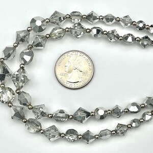 May include: Two strands of clear, faceted beads with silver-toned metal accents. The beads are various shapes, including round, diamond, and oblong. A US quarter coin is included for size reference. The jewelry is displayed on a white background.