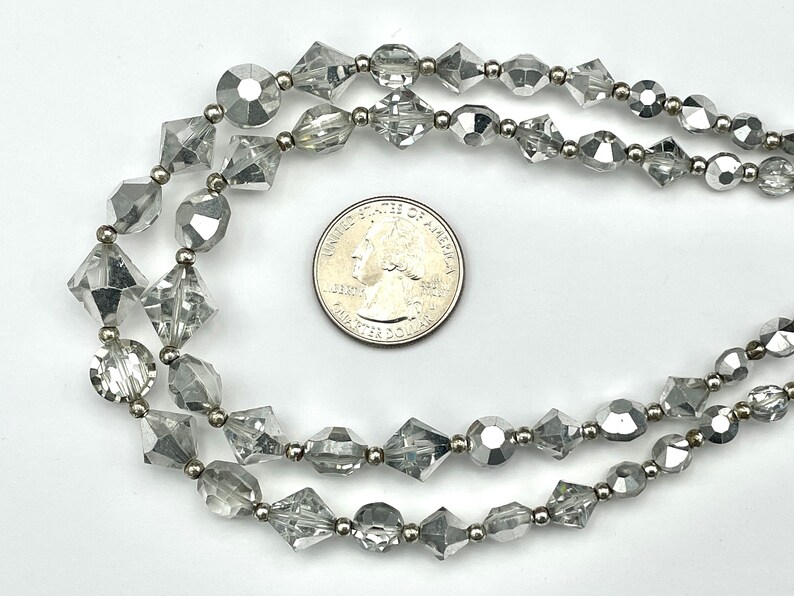 May include: Two strands of clear, faceted beads with silver-toned metal accents. The beads are various shapes, including round, diamond, and oblong. A US quarter coin is included for size reference. The jewelry is displayed on a white background.