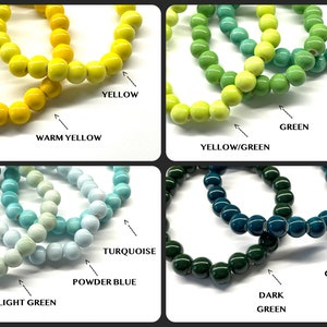 May include: A set of ten bracelets with different shades of green, blue, and yellow. The bracelets are made of round ceramic beads.