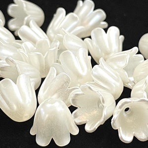 May include: A group of white plastic flower beads with a pearlescent finish. The beads are shaped like a bell with five petals.