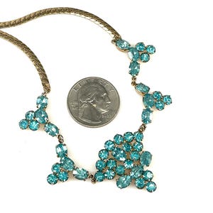 May include: A gold chain necklace with a cluster of turquoise blue rhinestones in a cascading design.