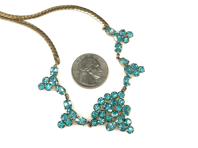 May include: A gold chain necklace with a cluster of turquoise blue rhinestones in a cascading design.