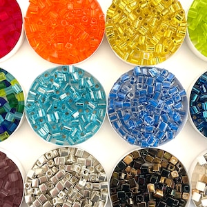 May include: Assortment of colorful square glass beads in small containers. The beads are in various colors, including red, orange, yellow, green, blue, purple, silver, and black.
