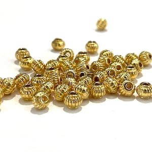 May include: A pile of gold-colored metal beads with a textured, ribbed surface. The beads are round and have a hole in the center for stringing.