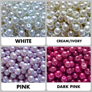 May include: A collection of round, smooth, faux pearl beads arranged in four distinct color groups labeled as white, cream/ivory, pink, and dark pink. Each bead features a central hole for stringing, showcasing a glossy, reflective finish.