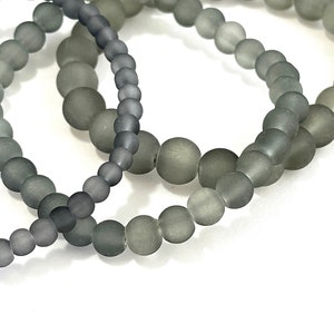 May include: Two gray beaded bracelets with a frosted finish. The bracelets are made of round beads and are stacked on top of each other.