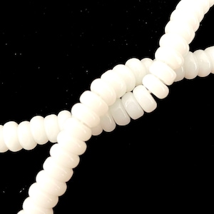 May include: A strand of white glass beads, each bead is round and slightly elongated, creating a textured look. The beads are strung together to form a long necklace or bracelet.
