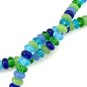 May include: A strand of colorful glass beads in shades of blue, green, and light blue. The beads are round and have a smooth, polished finish.