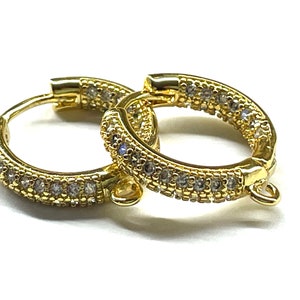 May include: A pair of gold hoop earrings with a clear crystal pave design. The earrings have a hinged closure.