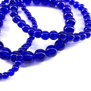May include: Three strands of blue glass beads, each strand is a different size, the beads are round and smooth.